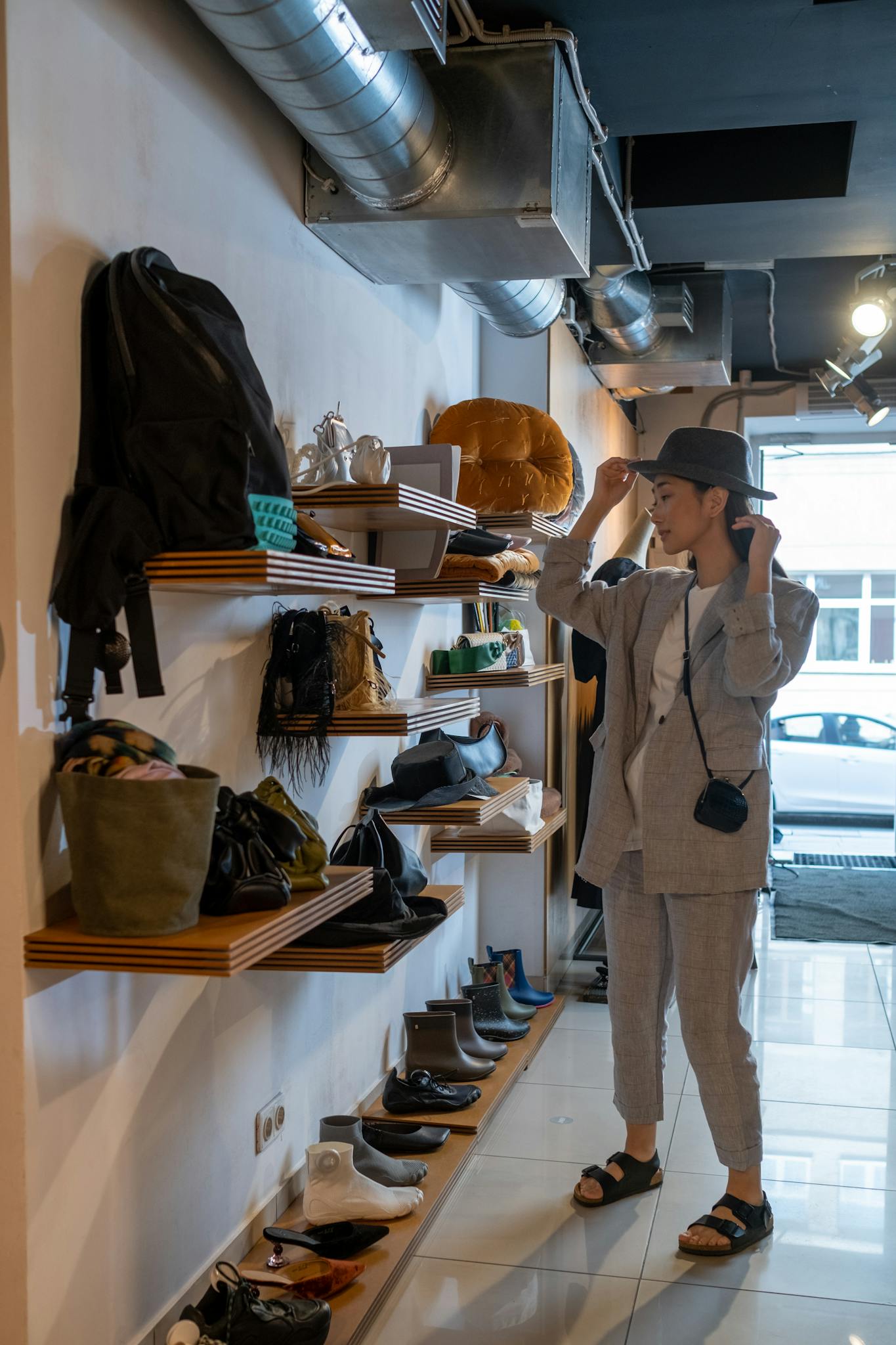 Asian woman shopping for a hat in a stylish boutique with assorted accessories.